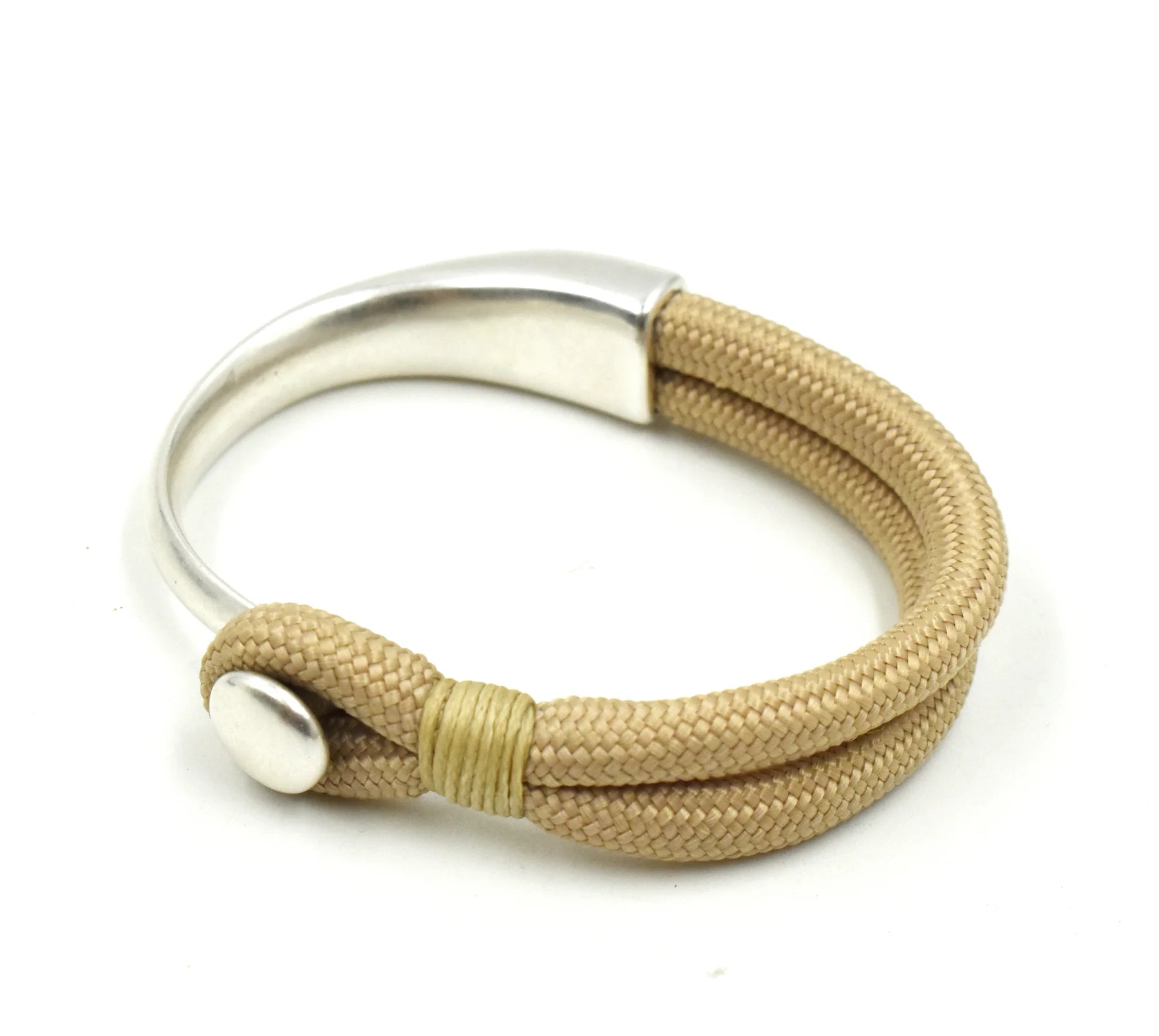 A silver-toned metal cuff bracelet with a textured tan woven cord wrap, featuring a silver snap closure and a thin gold accent wrap near the clasp.