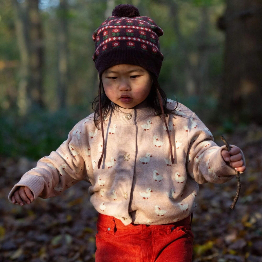 Child wearing a patterned hat and light sweater in a forest setting