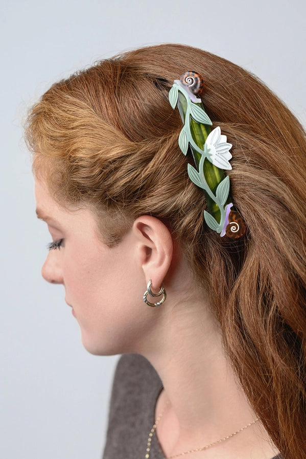 Woman with hair styled with a decorative hair clip featuring leaves and flowers on a plain background