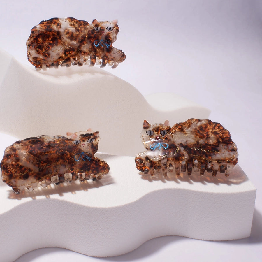 Three tortoiseshell cat-shaped hair clips on a white stand with a white background