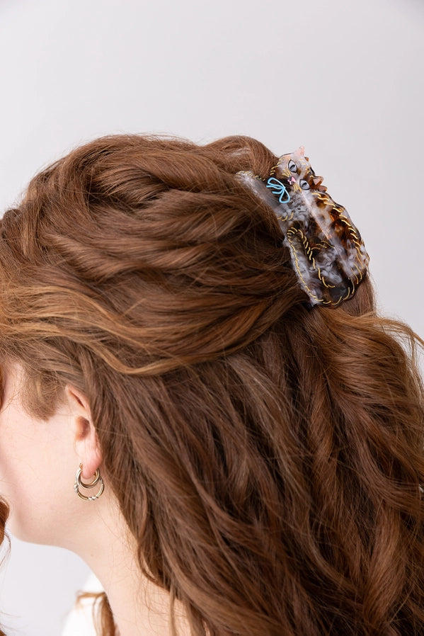 Close-up of a person with braided hair wearing a decorative cat shaped hair clip against a neutral background