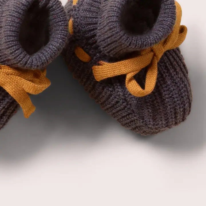 Pair of dark gray knitted baby booties with mustard yellow laces.