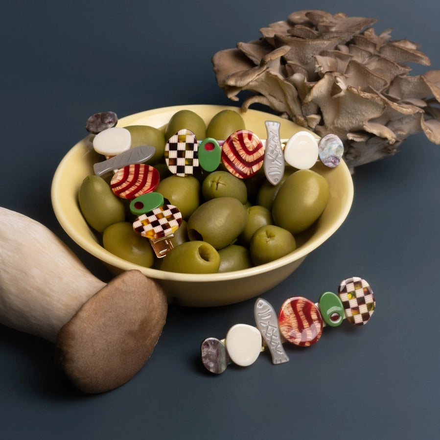 Food themed hair clips sit within a bowl of green olives against a dark surface