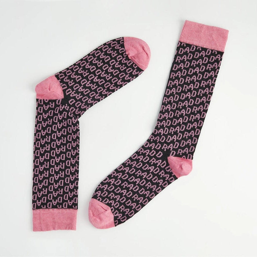 A pair of dark socks with a repeating pink monogram pattern and solid pink toe, heel, and cuff sections, displayed on a clean white background.
