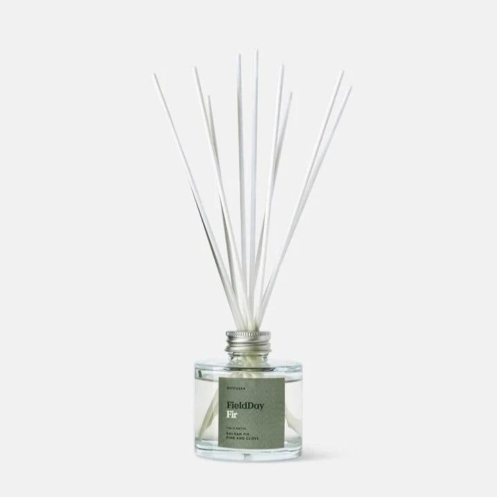 Field Day Fir reed diffuser in a clear glass bottle with silver cap and white reeds.