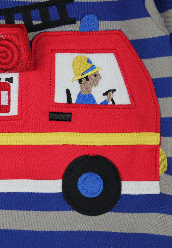 Close-up of a red fire truck applique on a blue and gray striped garment, featuring a firefighter character in the window and a black wheel with a blue center.