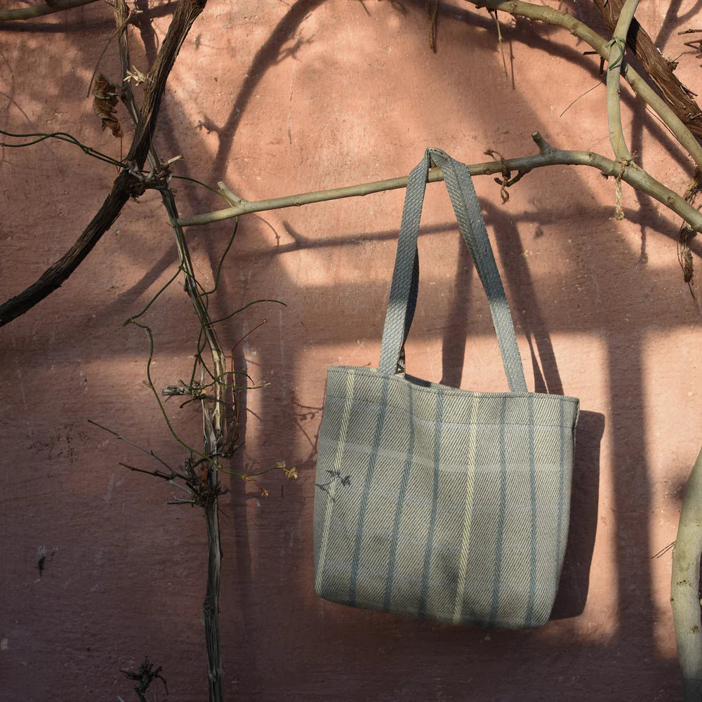Gray and beige striped tote bag hanging on a branch.