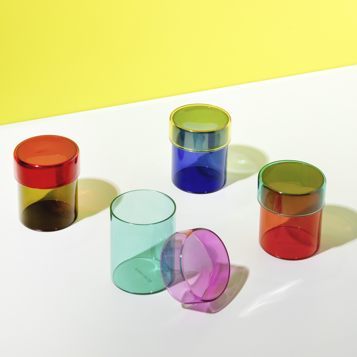 Set of colorful transparent tumblers on a white surface with a yellow background