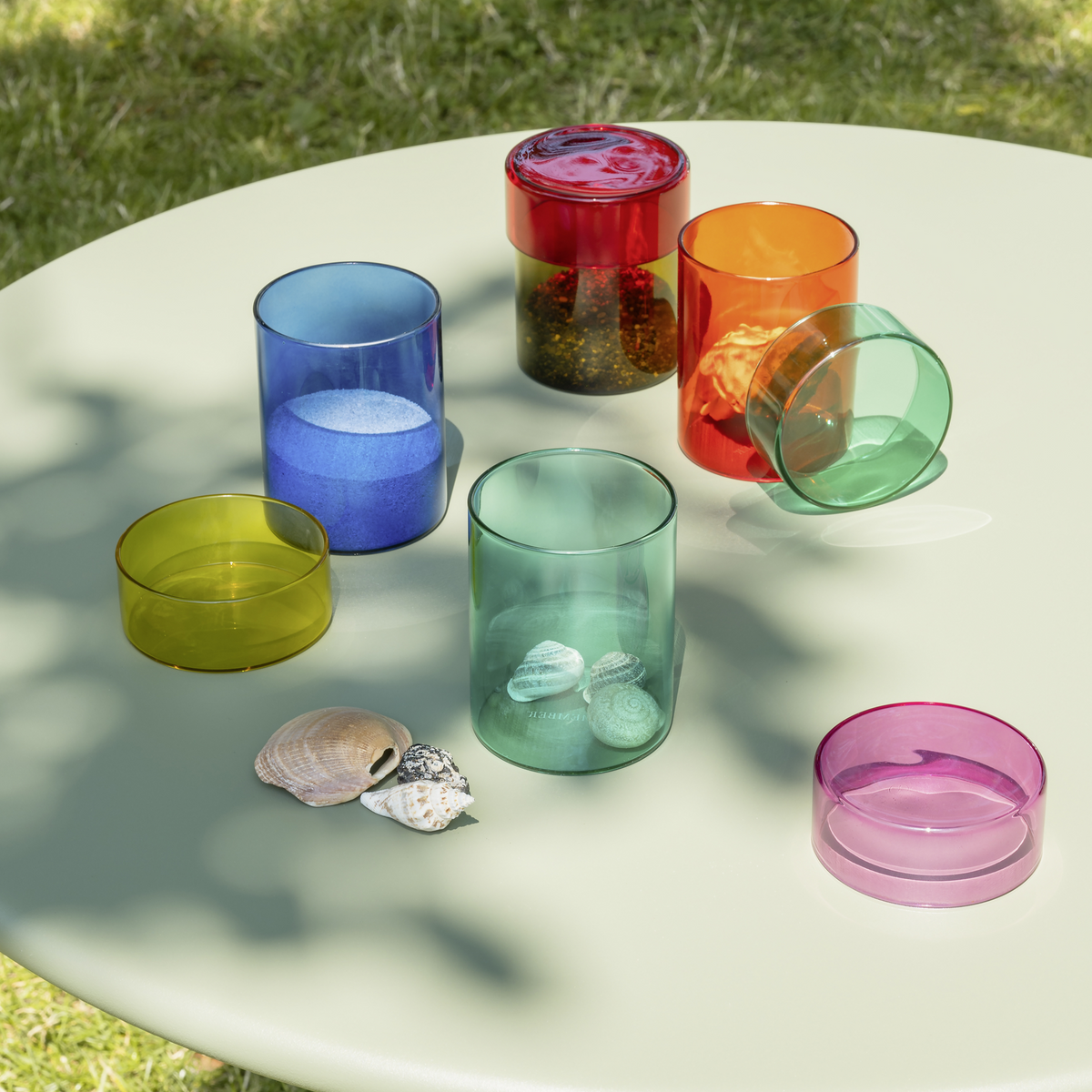 Colorful glass tumblers on a white surface with grass in the background