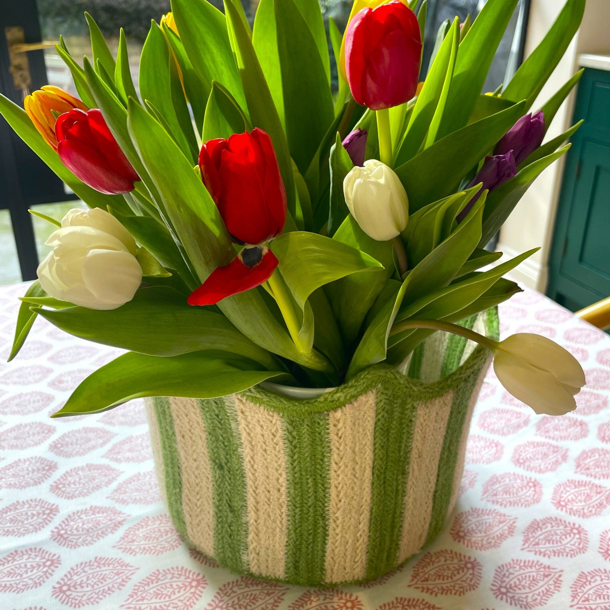 A bouquet of colorful tulips in a green and cream striped knitted vase.