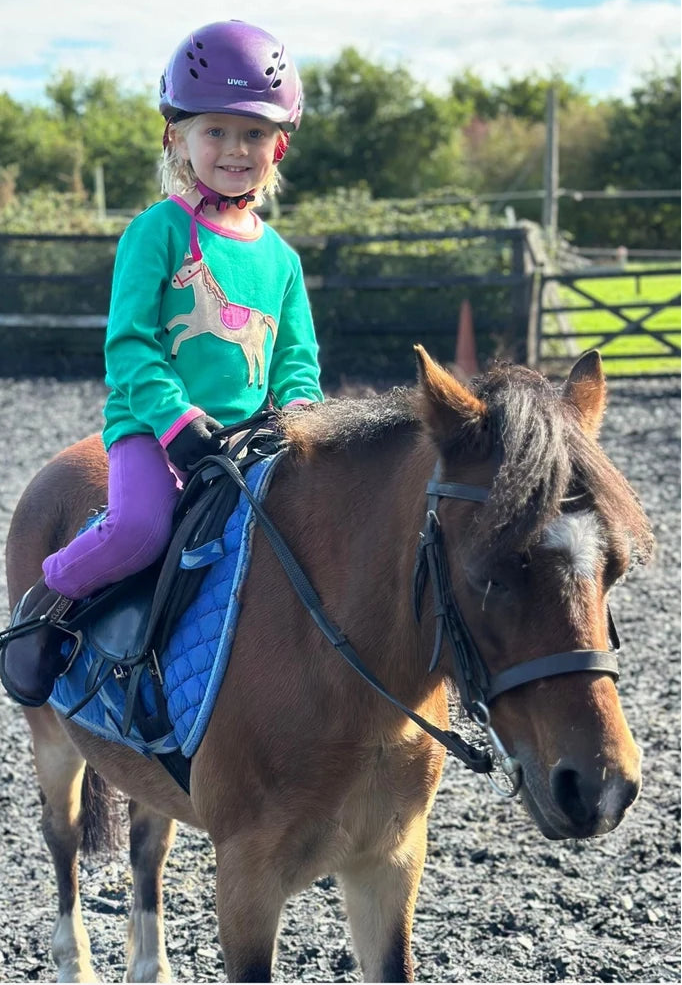 Young girl riding a pony in an outdoor equestrian setting