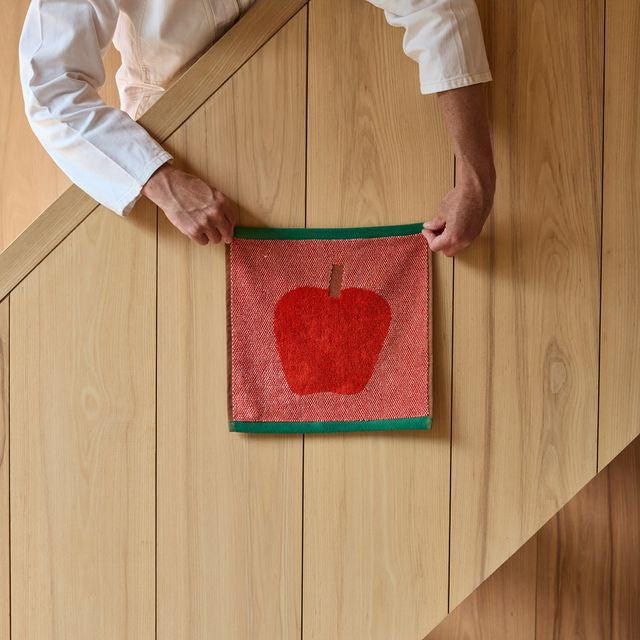 Person holding a red apple-themed towel on a wooden surface