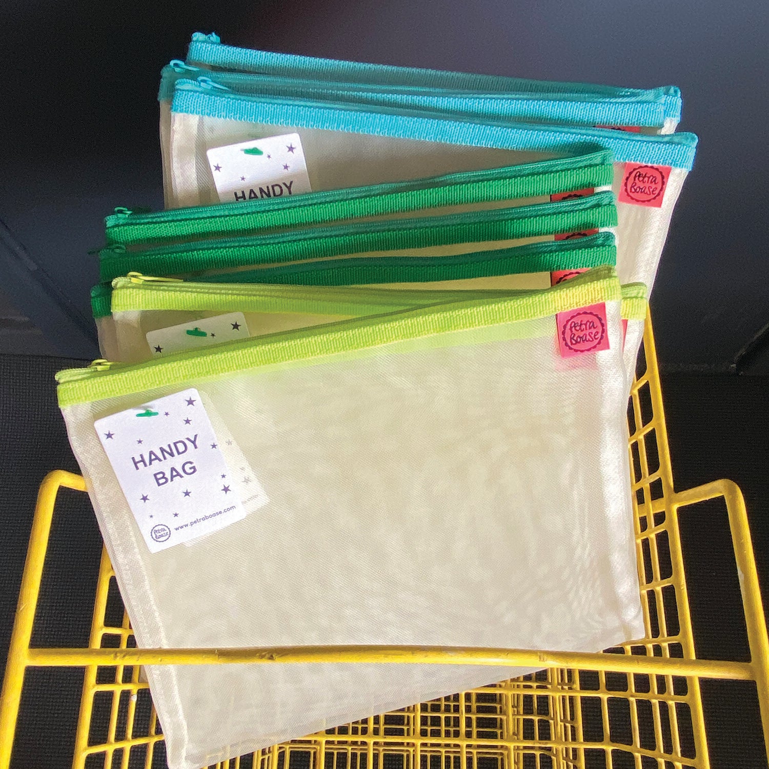 Stack of mesh "Handy Bags" with teal, green, and lime zippers. Each bag has a small label.