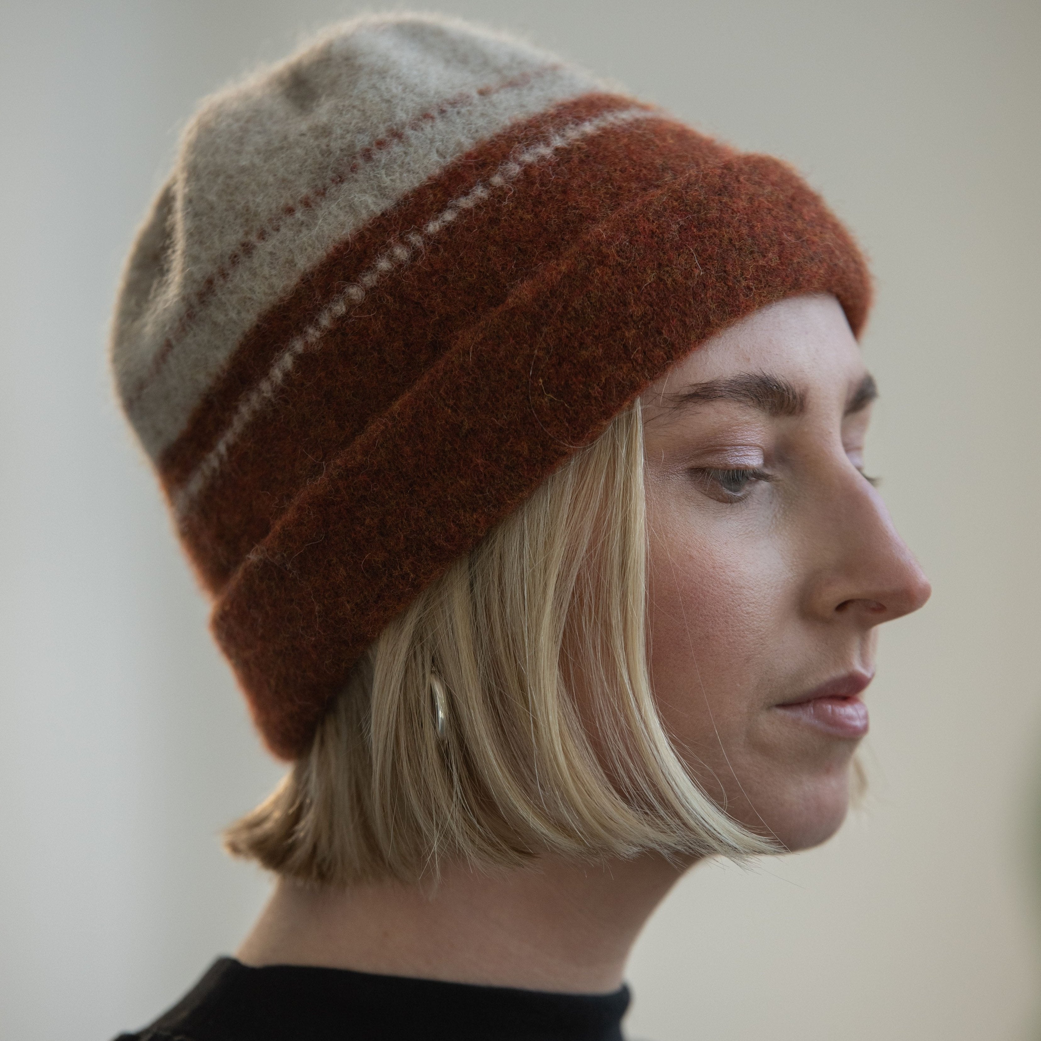 A rust and beige hand-knitted beanie with subtle horizontal stripes.  The wool is thick and textured.