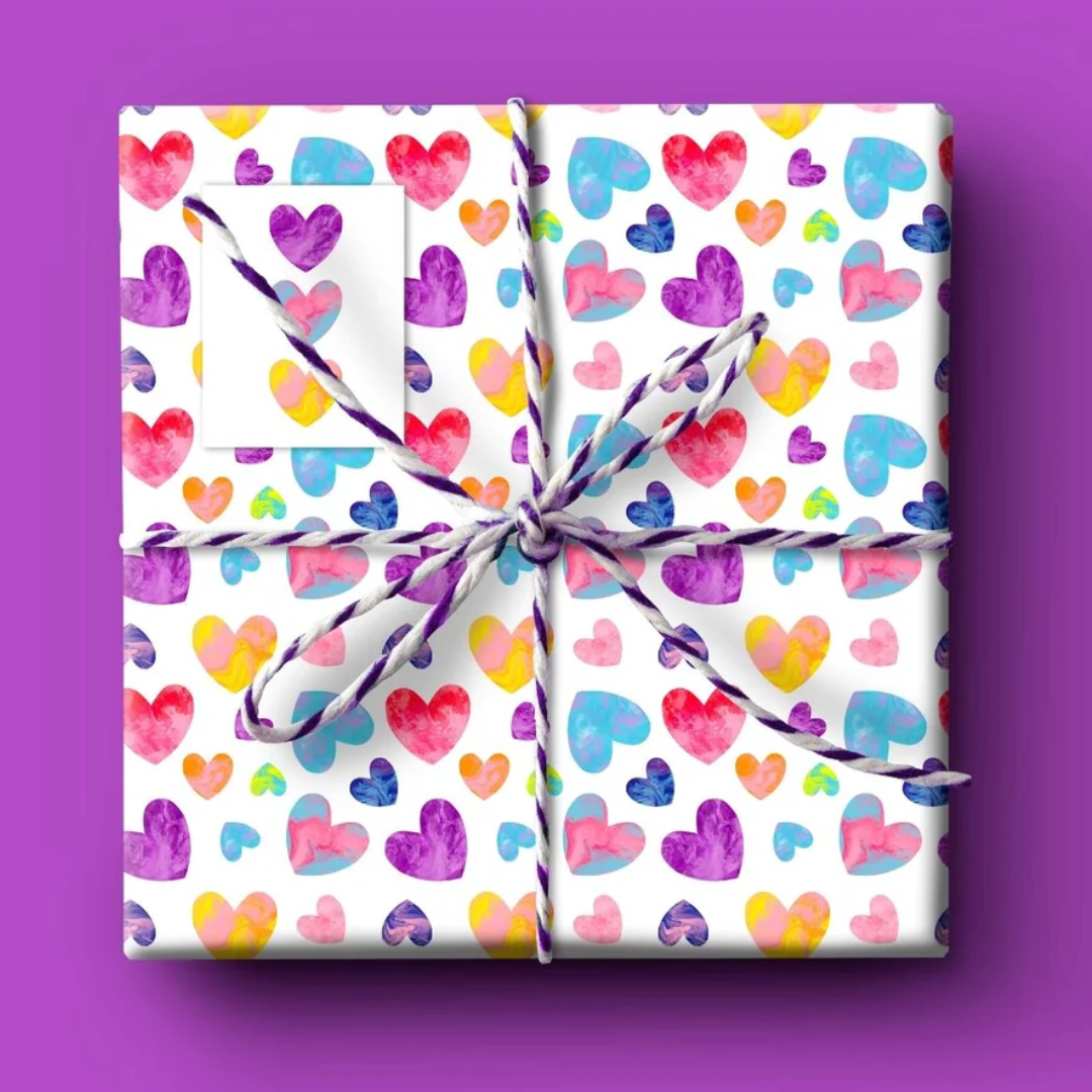 Square gift wrapped in white paper with a colorful watercolor heart pattern, tied with twine.