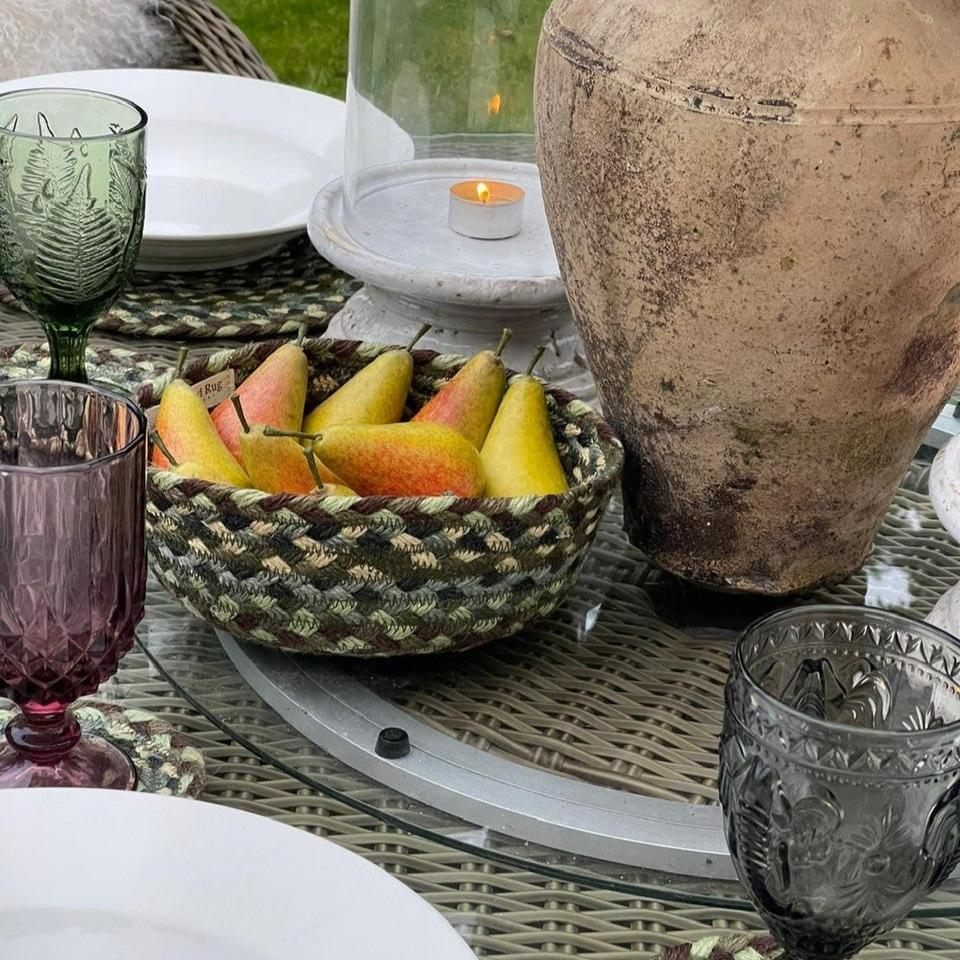 A woven bowl filled with artificial pears sits on a glass-topped outdoor table.