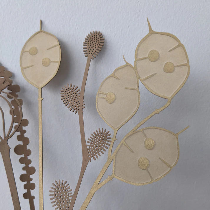 Intricate beige and brown paper cut-out artwork depicting stylized botanical forms, including seed pods and flower heads.