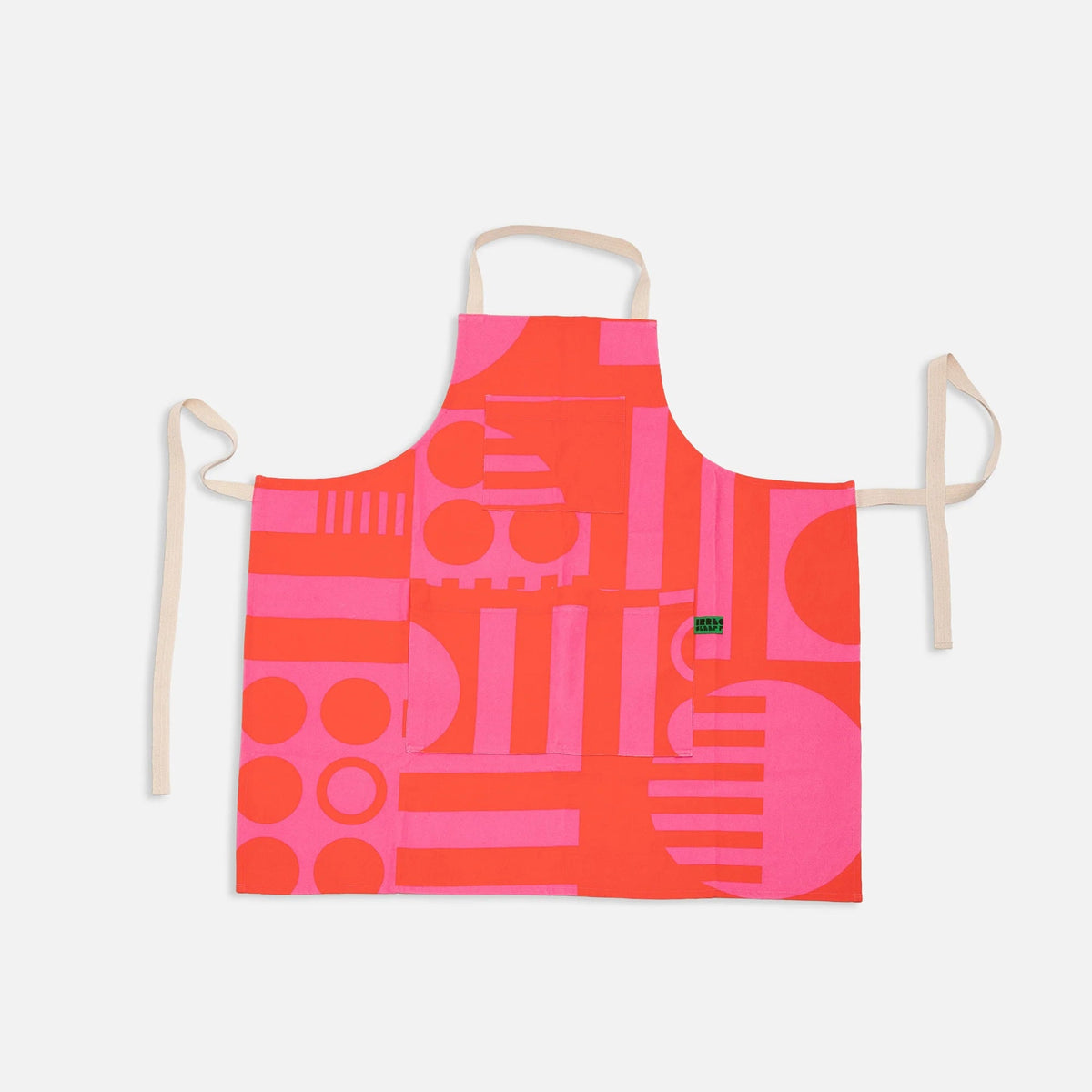A cotton apron with a vibrant pink and orange geometric pattern, featuring cream-colored neck and waist ties, displayed against a light gray background.