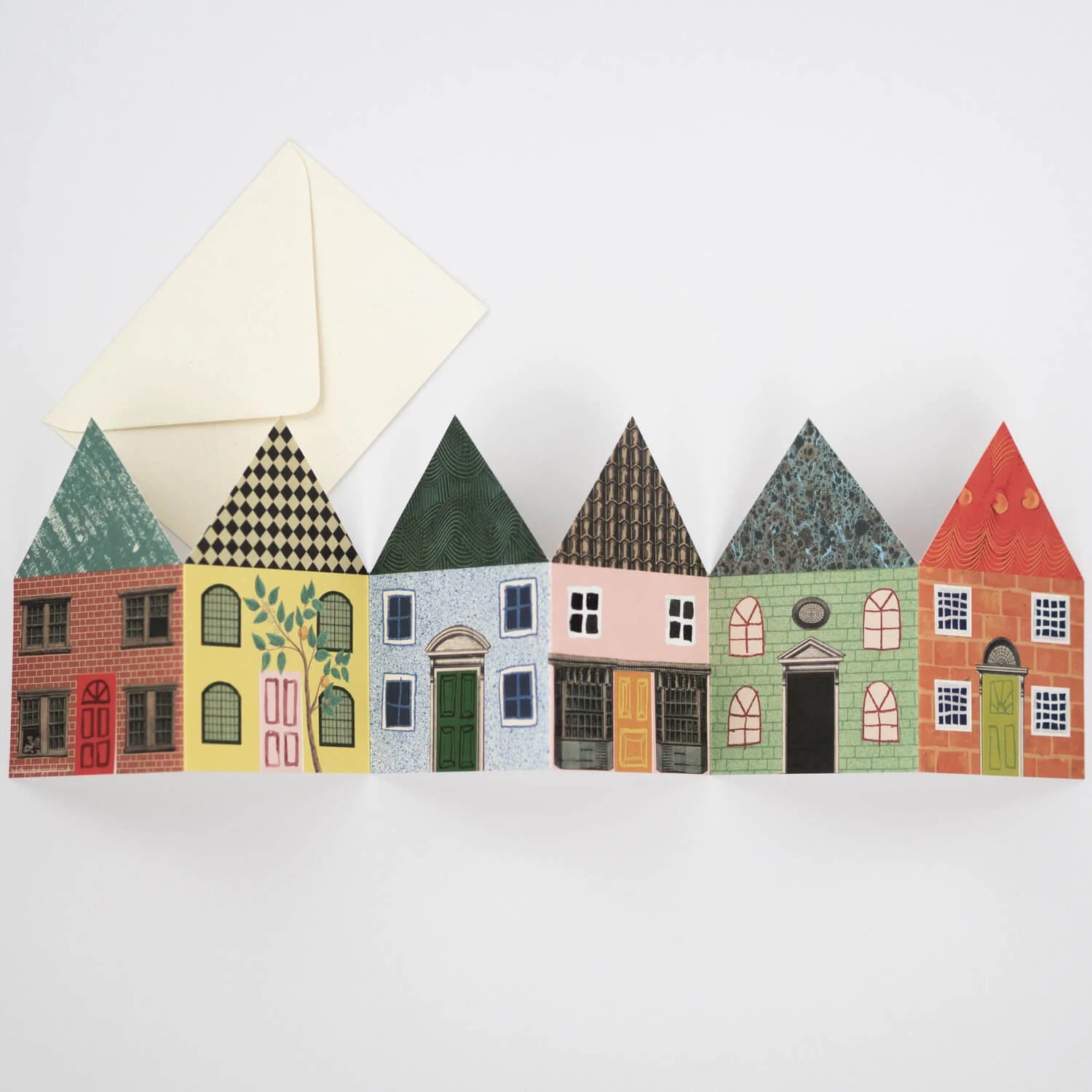 Row of six small, colorful paper houses with various architectural details.  A cream envelope is partially visible above.