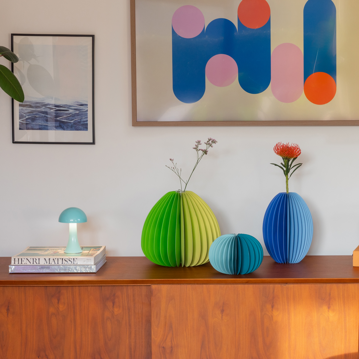 Colorful paper vases on a wooden surface with abstract art in the background