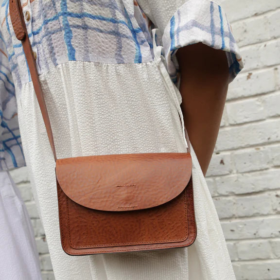 A small, brown leather crossbody bag with a flap closure.  The leather has a textured appearance.