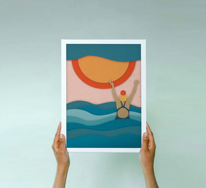 Paper-cut style art print depicting a swimmer emerging from ocean waves beneath a large sun.