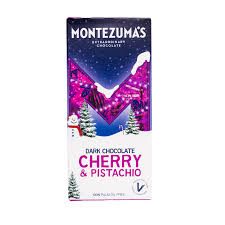 A package of Montezuma's Extraordinary Chocolate Dark Chocolate Cherry & Pistachio, featuring a festive winter-themed design with a large purple 'M' on a snowy mountain under a dark blue starry sky.