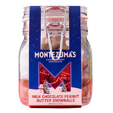 A glass clamp-lid jar of Montezuma's Extraordinary Chocolate Milk Chocolate Peanut Butter Snowballs, featuring a blue and red festive label with a snowman and Christmas trees.