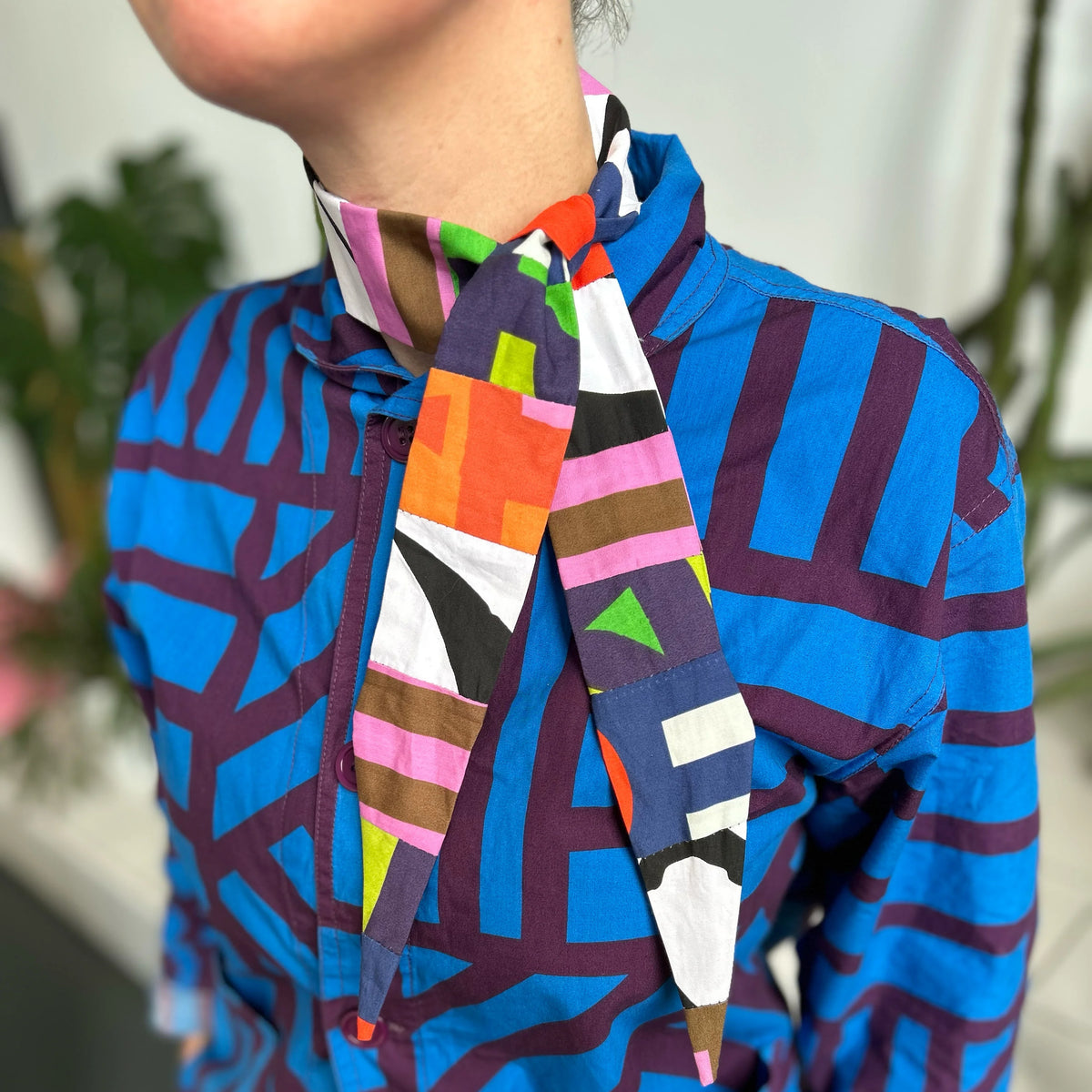 A close-up of a person wearing a vibrant blue and purple geometric patterned shirt with a colorful abstract print neck scarf tied around the collar.