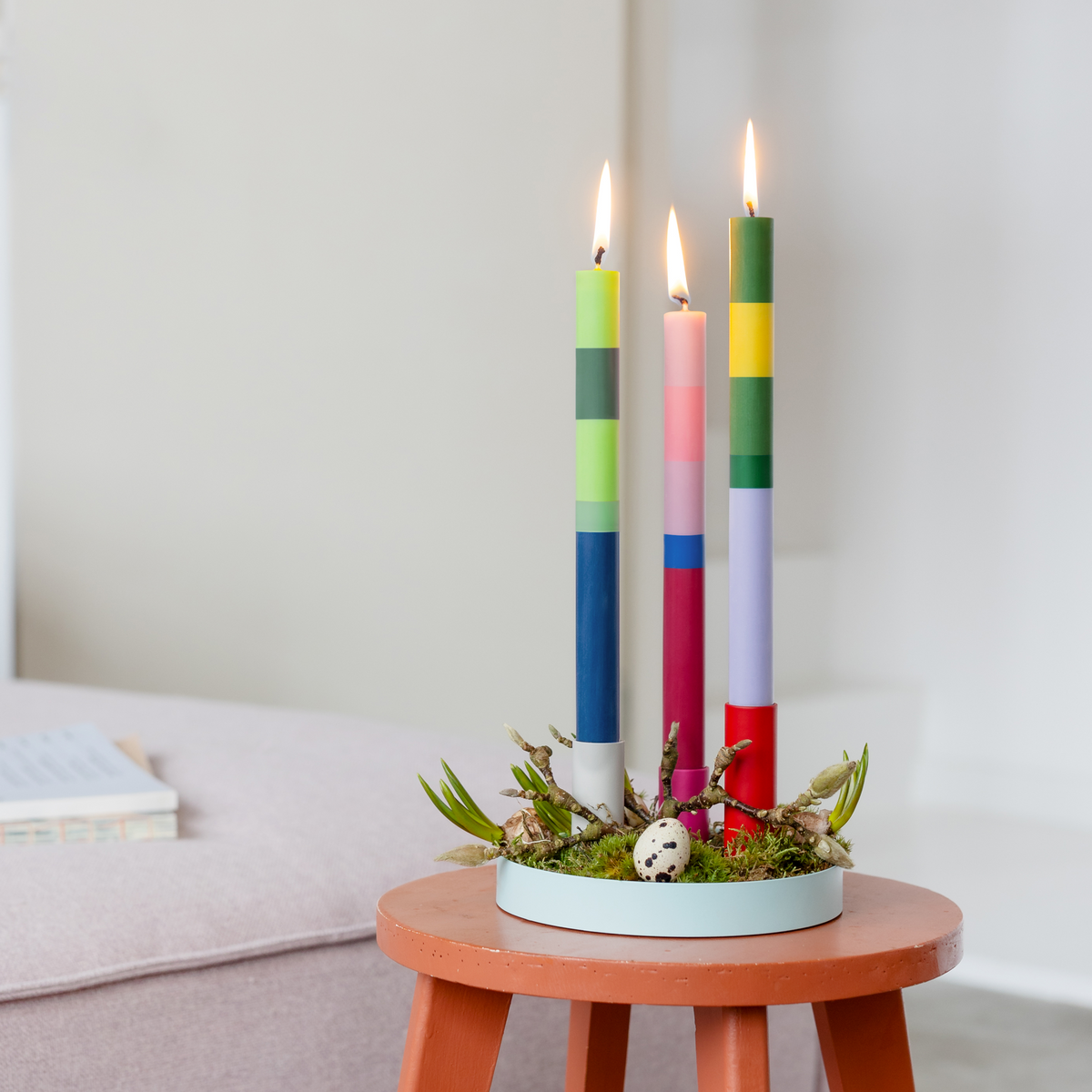 Colorful candles in a decorative holder on a small round table with a neutral background
