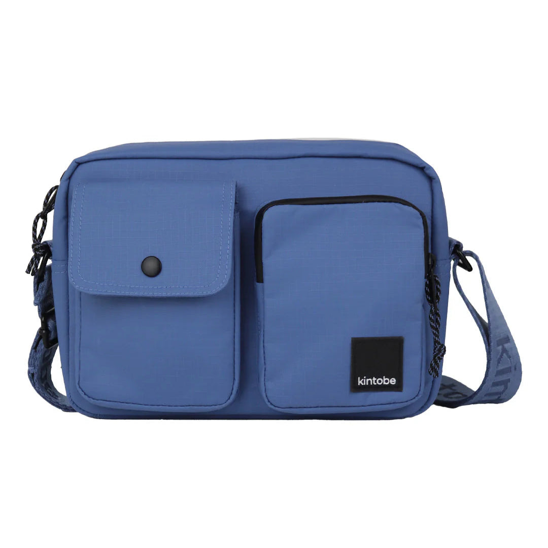 Blue crossbody bag with two front pockets and adjustable strap.  Features a small brand label.