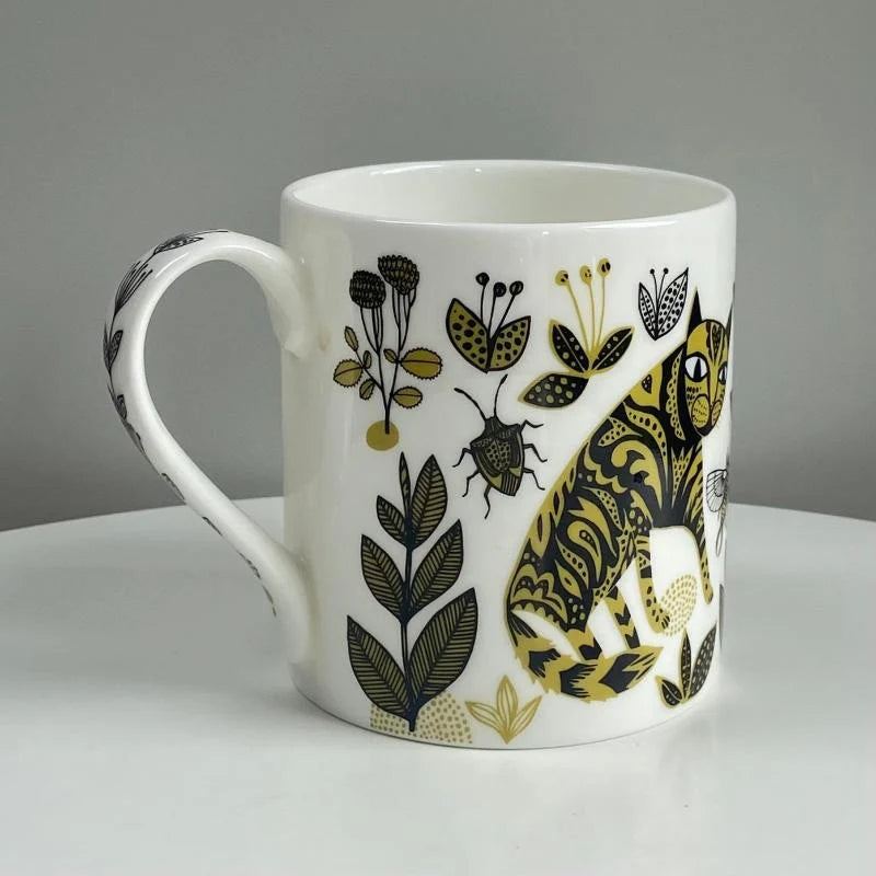 White mug with black and gold floral and animal design on a gray background