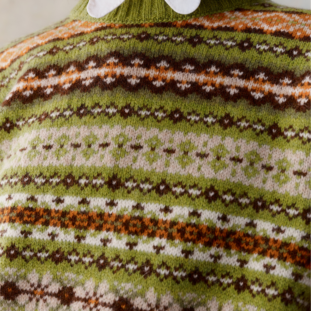 Close-up of a green wool sweater with a Fair Isle pattern in brown, cream, and orange.