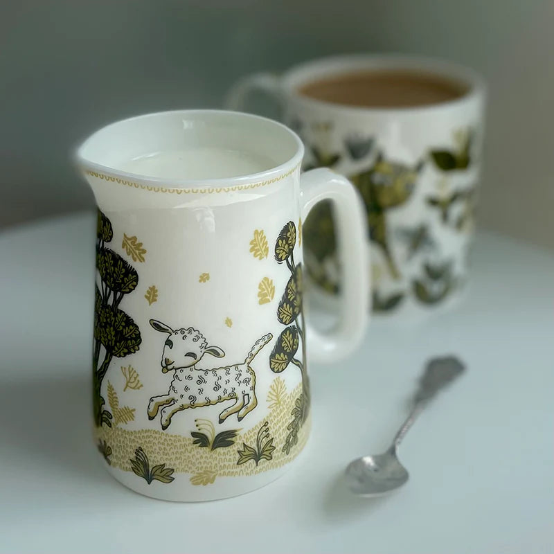 Creamer with a playful lamb design in gold and dark green on a white background.