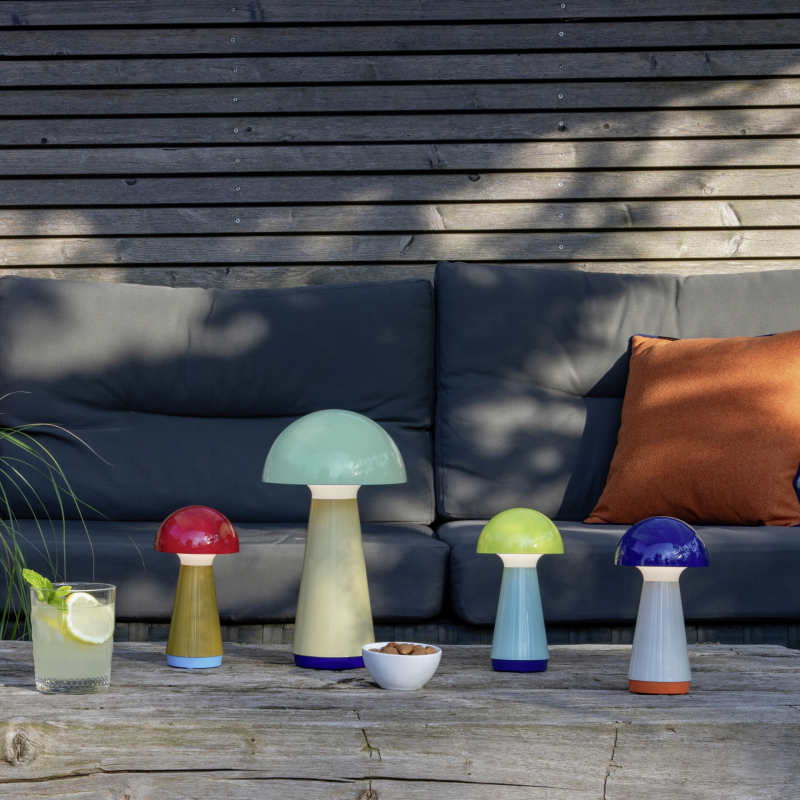 Colorful mushroom-shaped lamps on a wooden table with a gray sofa and plant in the background