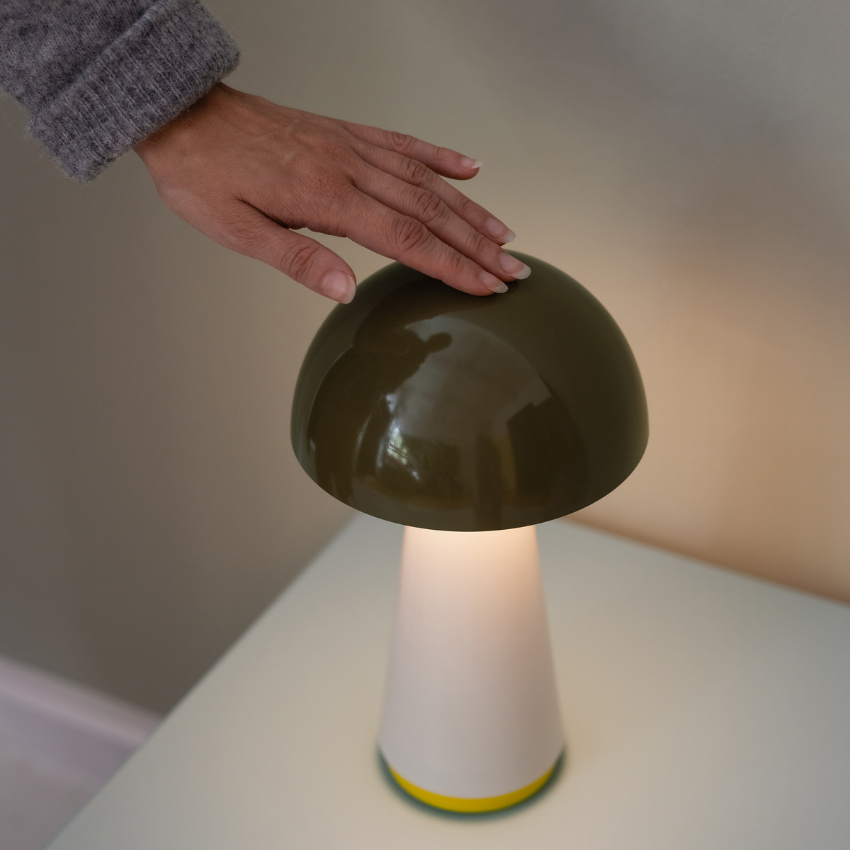 Mushroom-shaped lamp with a hand touching its cap on a neutral background