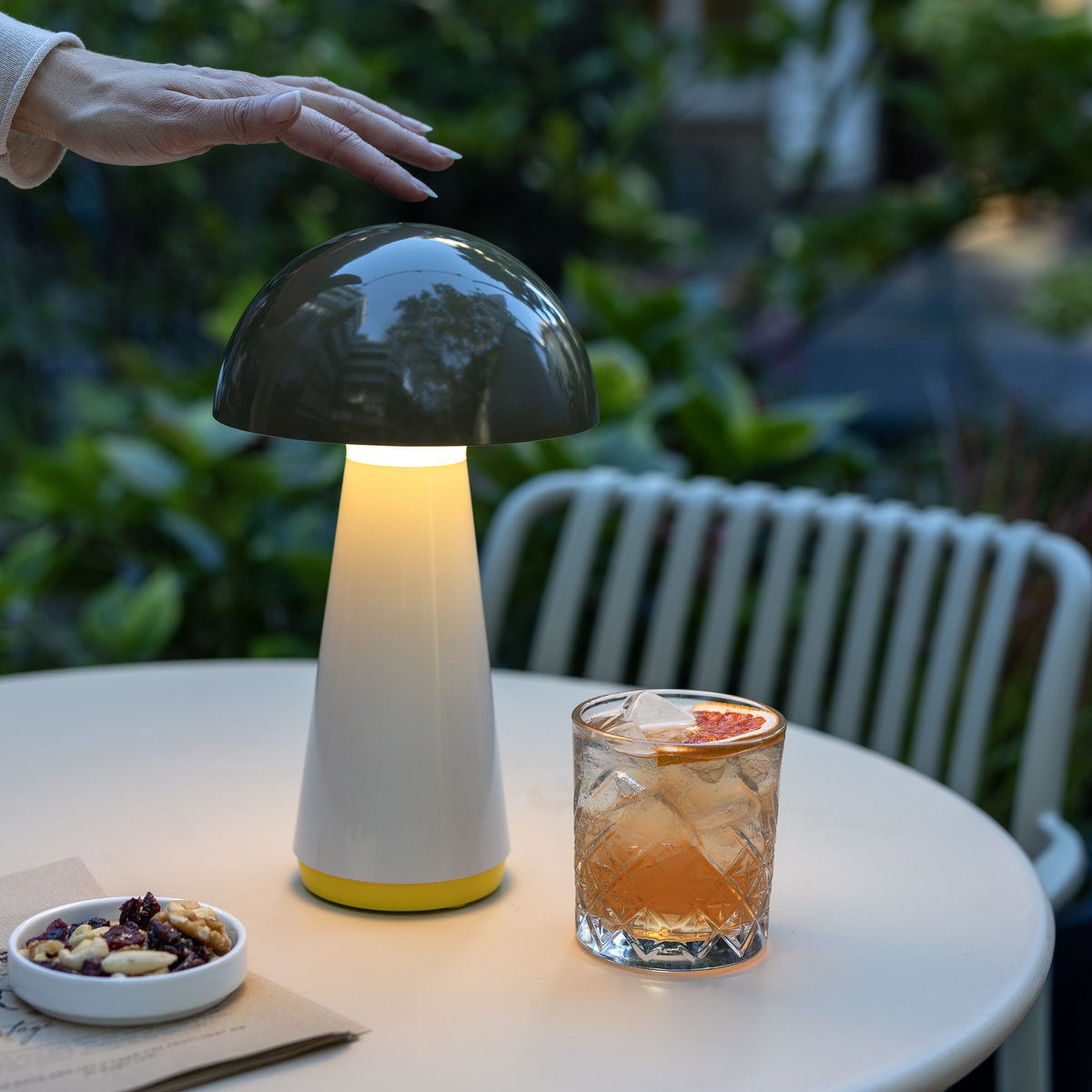 Mushroom-shaped lamp on a table with a drink and snacks, outdoors.