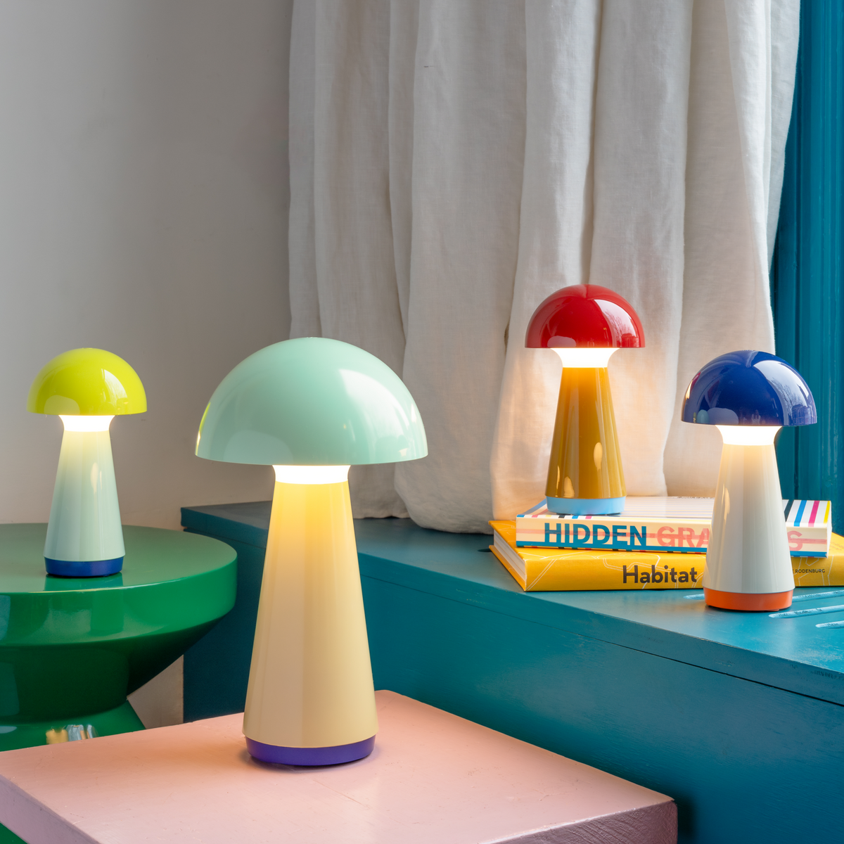 Colorful mushroom-shaped lamps on a shelf with books in a room setting.