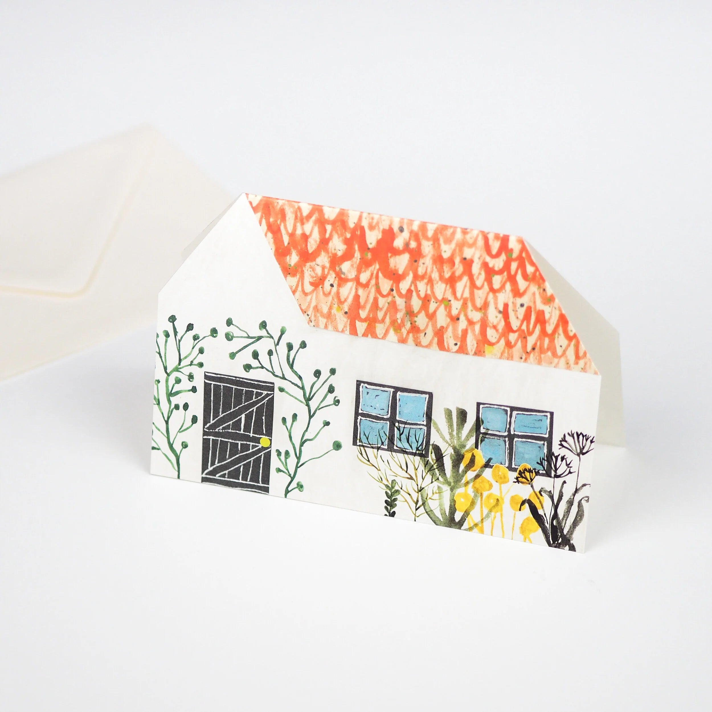Illustrated paper house card with orange roof, black door, blue windows, and green and yellow floral details.