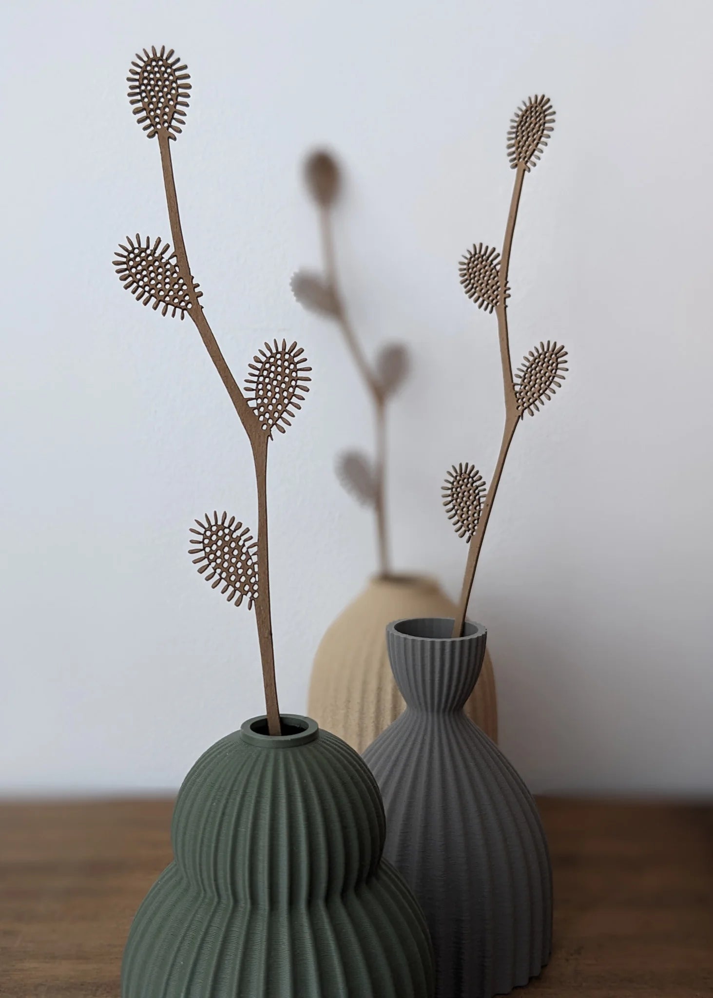 Brown laser-cut wood branch with textured, oval-shaped leaves in ribbed vases.