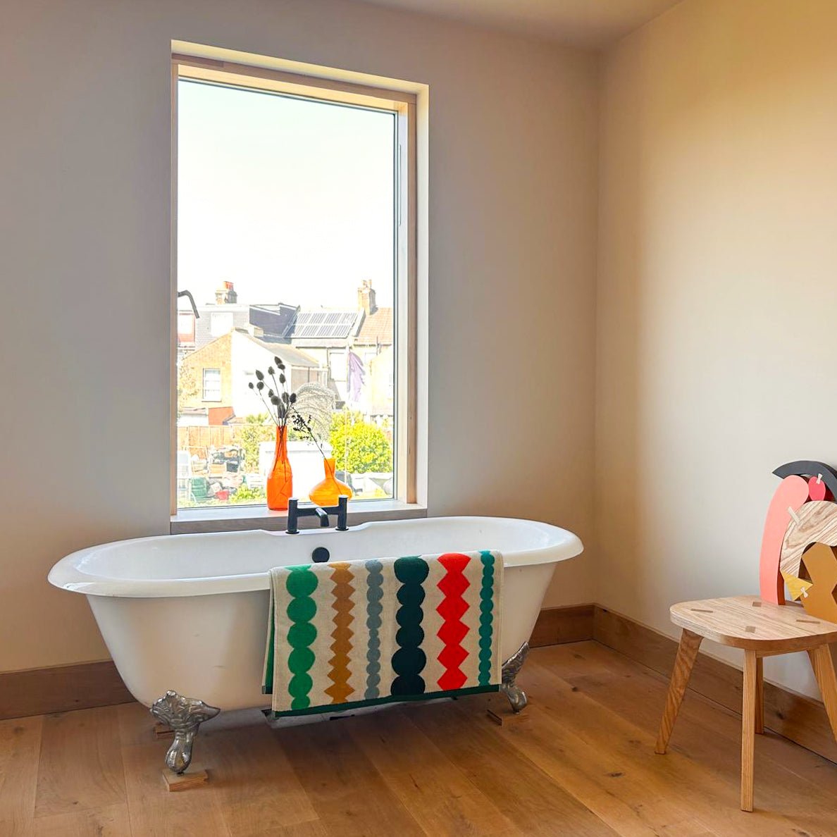 A bright bathroom featuring a white bathtub with a colorful Donna Wilson towel in green, red, and brown.