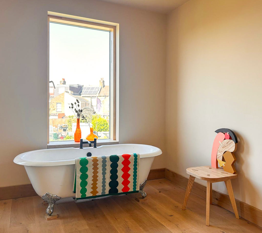 A bright bathroom featuring a white bathtub, a multi-colored striped towel by Donna Wilson, and wood accents.