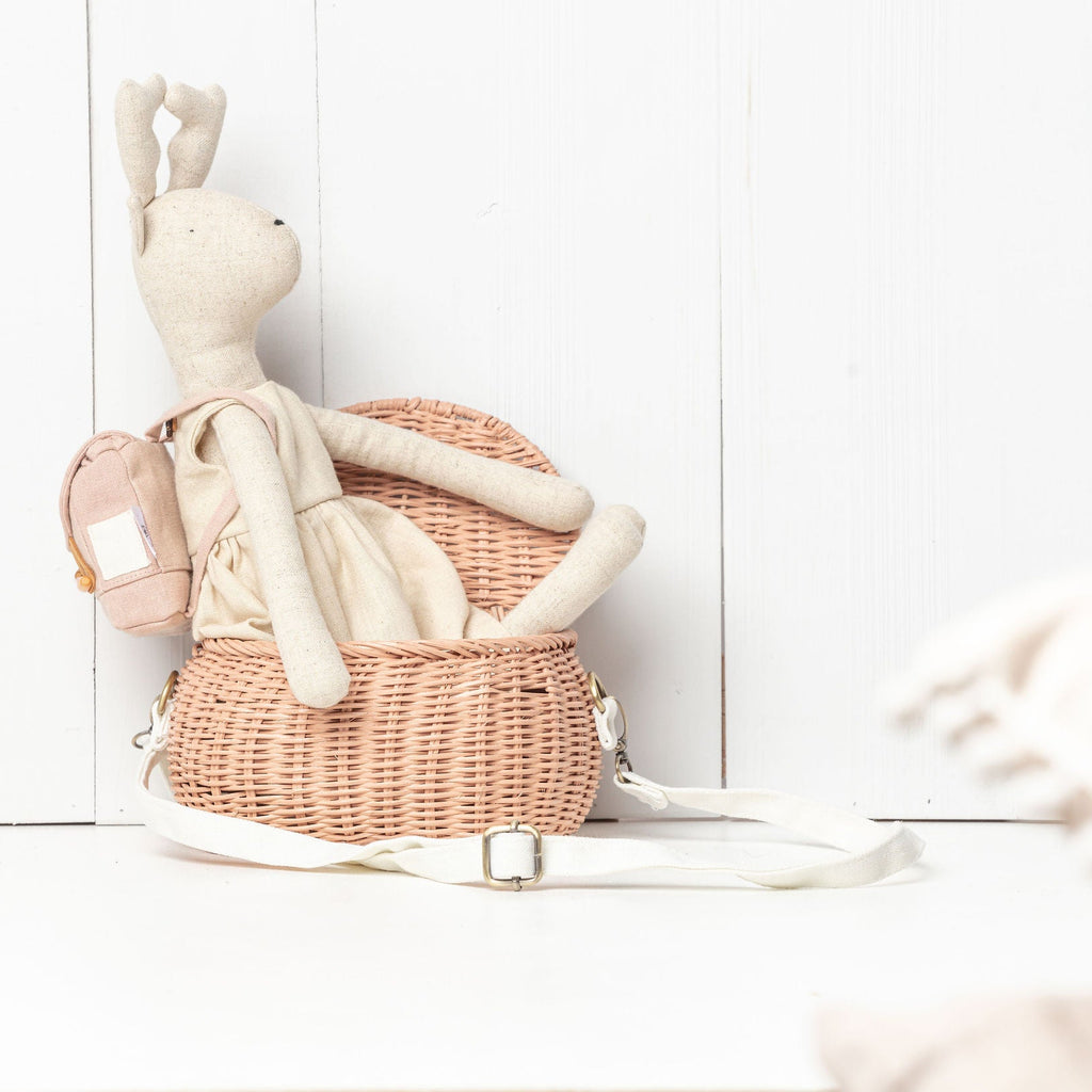 Stuffed rabbit toy with a pink backpack in a wicker basket on a white wooden floor.