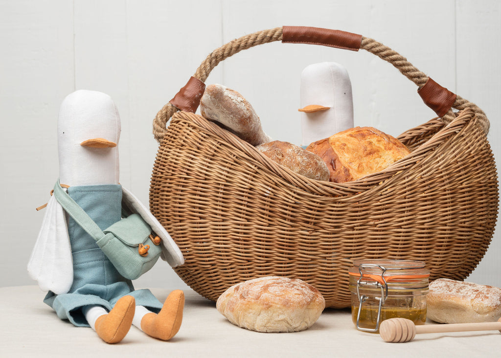Wicker basket with bread and a toy on a light background