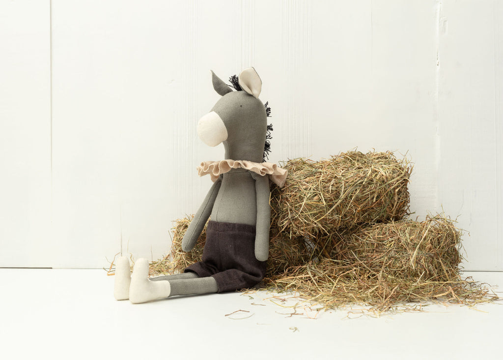Stuffed donkey toy sitting on a bale of hay against a white background