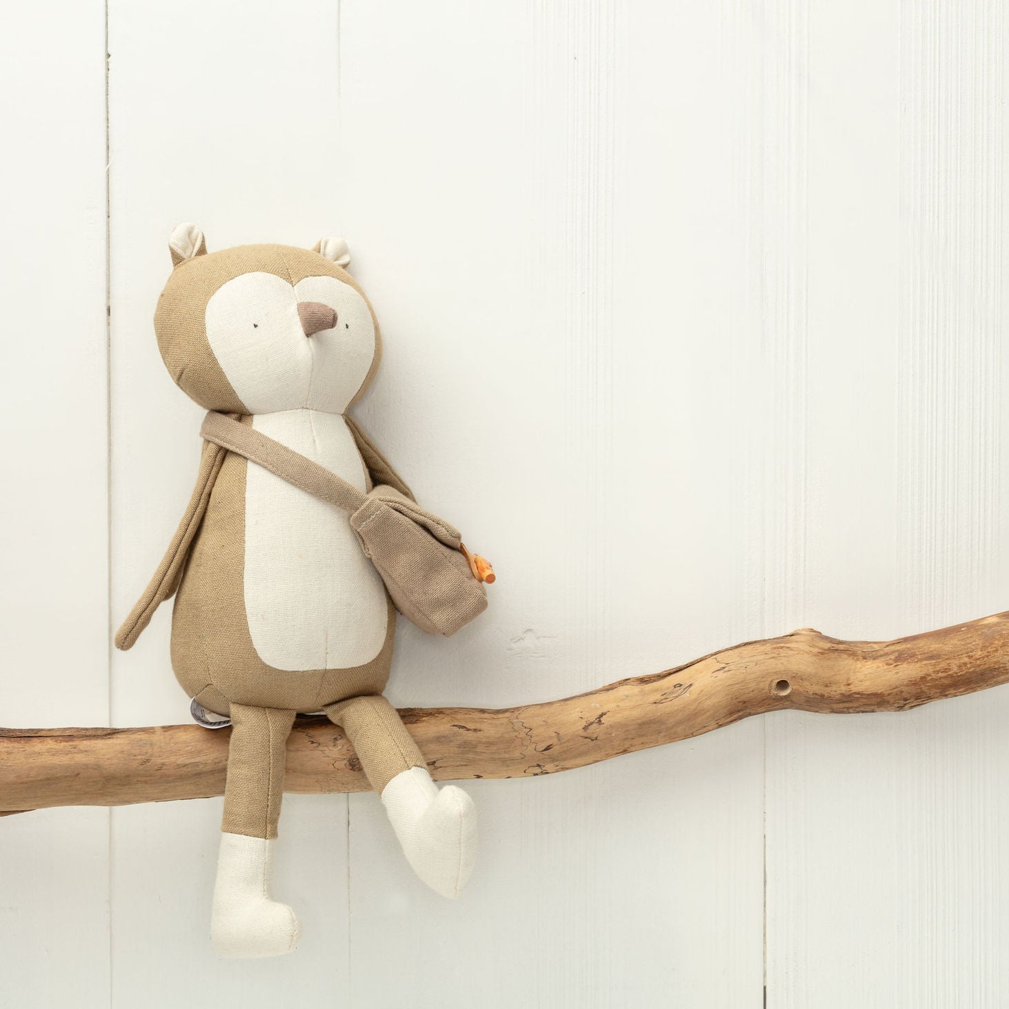 Stuffed animal toy resembling a bear with a backpack on a wooden branch against a light background
