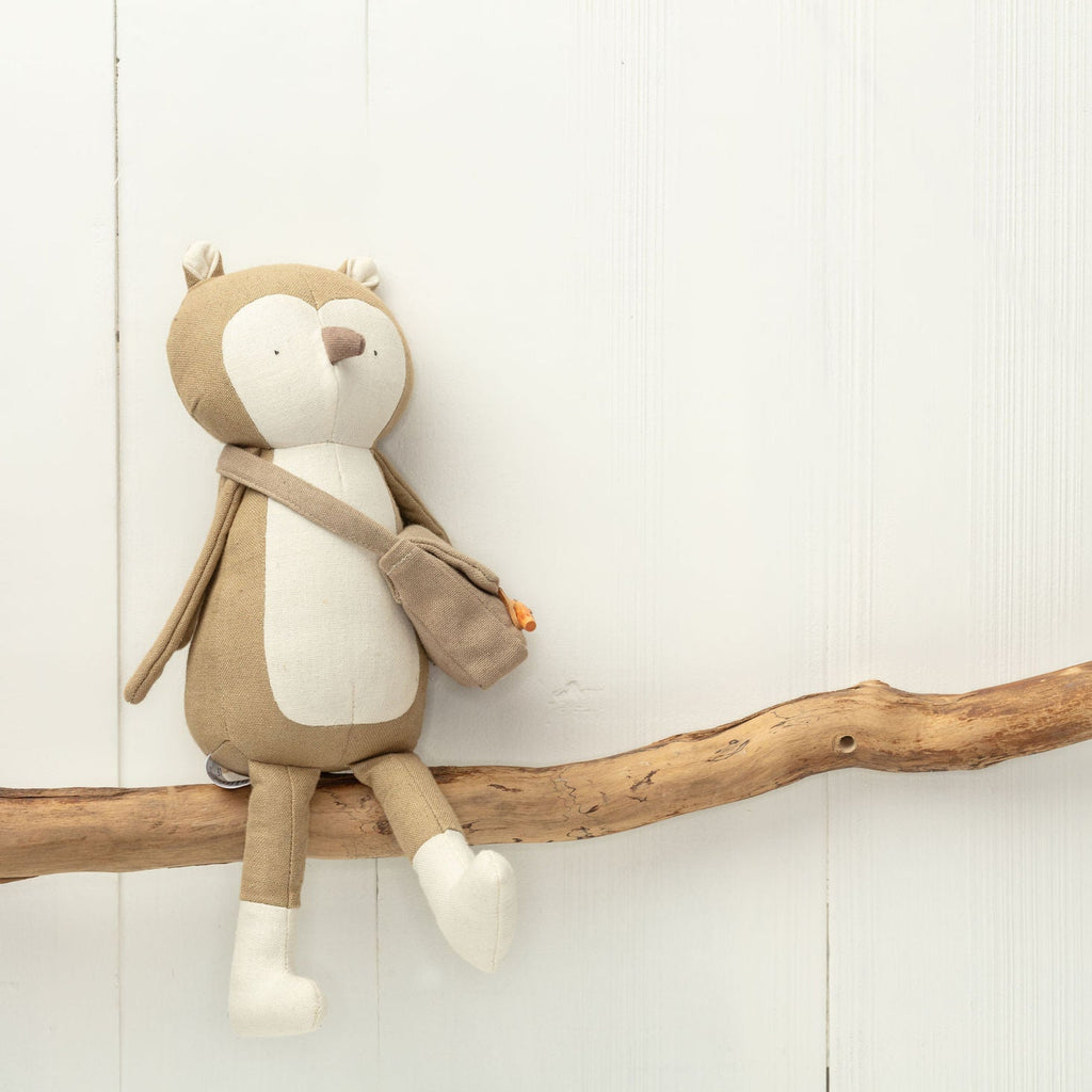 Stuffed animal toy resembling a bear with a backpack on a wooden branch against a light background