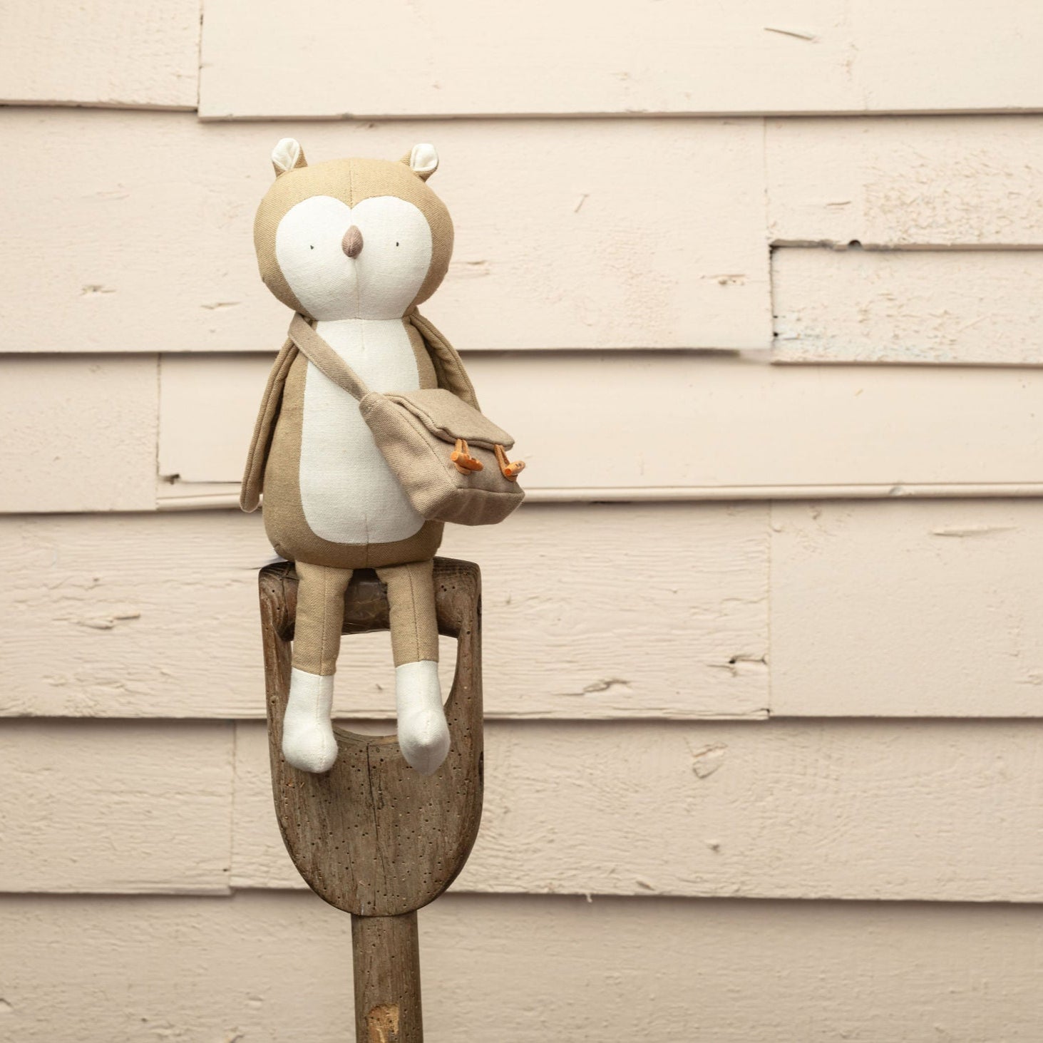 Toy owl  on a wooden stick against a beige wall.