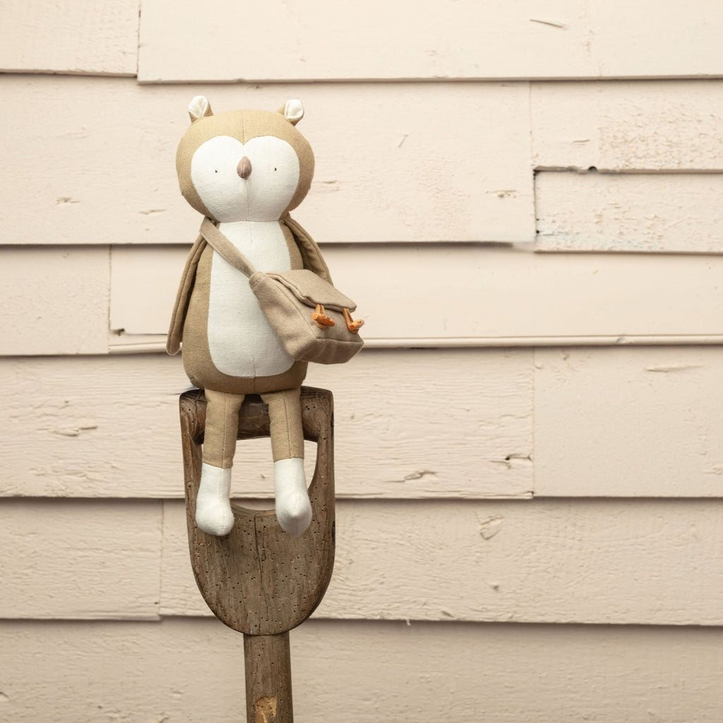 Toy owl  on a wooden stick against a beige wall.