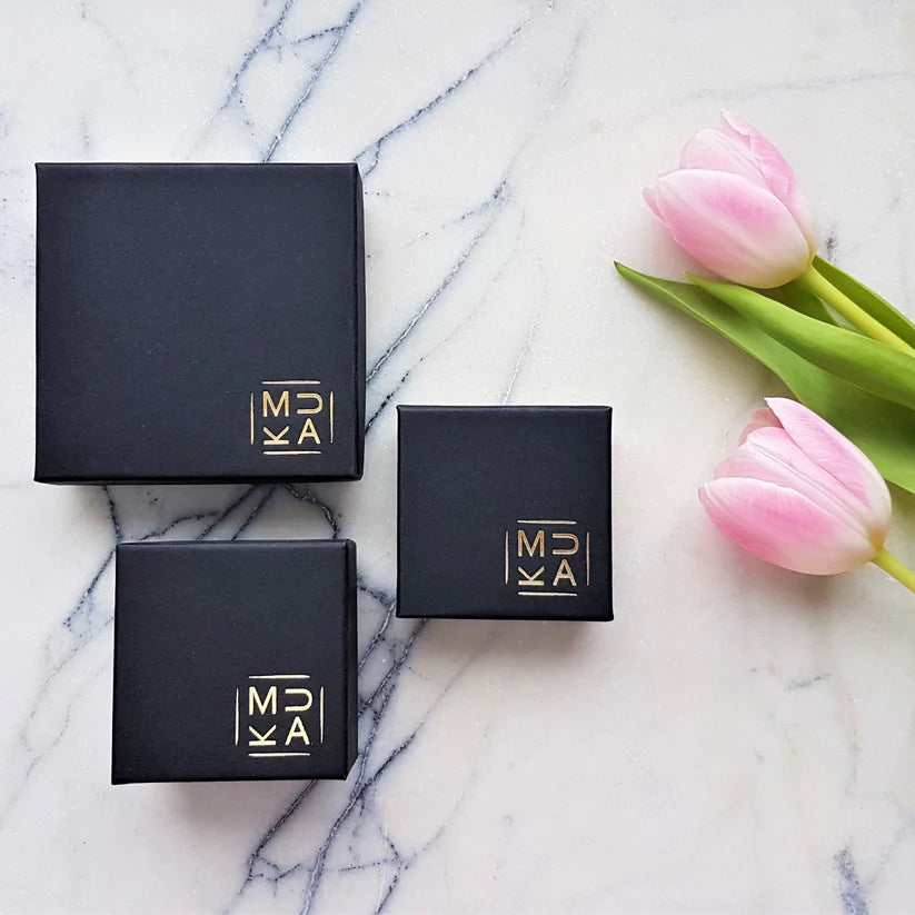 Three black square gift boxes with gold logo, varying in size.